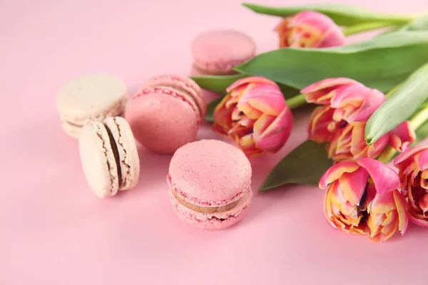 Delicious macarons and flowers on color background — Stock Photo, Image