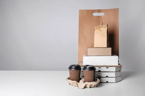 Verschillende pakketten en kartonnen bekers op tafel tegen een achtergrond met kleur. Levering foodservice — Stockfoto