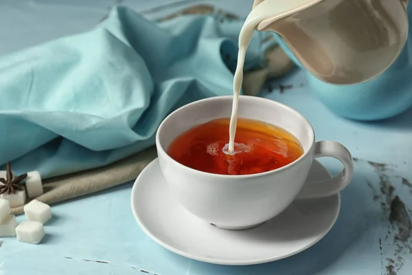 Наливаємо молоко в чашку гарячого чаю масала на столі — стокове фото