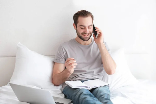 Homme freelance parler au téléphone tout en travaillant au lit — Photo