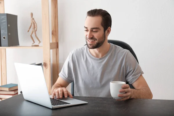 Male freelancer drinking tea while working with laptop in home office — Stock Photo, Image