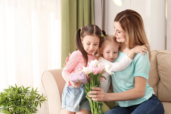 Мама получает подарок и цветы от своих милых маленьких дочерей дома — стоковое фото