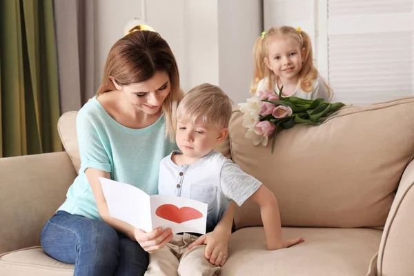 Mother receiving greeting card and flowers from her cute little children at home