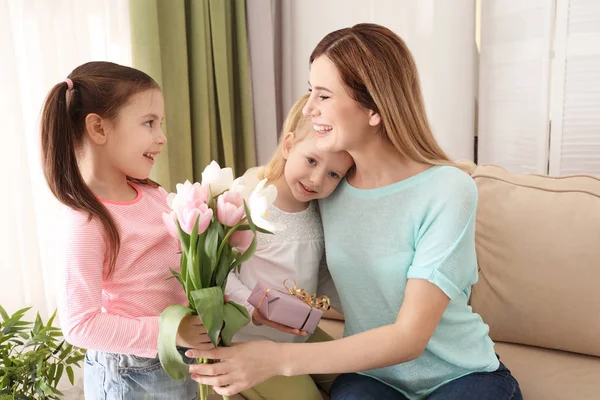 Mother receiving gift and flowers from her cute little daughters at home — Stock Photo, Image