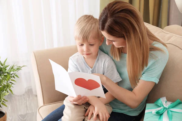 Mother receiving gift and greeting card from her cute little son at home — Stock Photo, Image