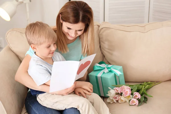 Mother receiving gift and greeting card from her cute little son at home — Stock Photo, Image