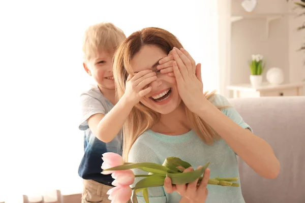 Schattig zoontje verrassend zijn moeder met bloemen thuis — Stockfoto