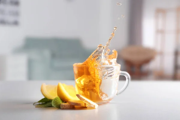 Splash na xícara de chá fresco com gengibre e limão na mesa da cozinha — Fotografia de Stock