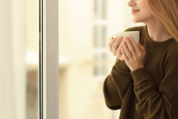 Mujer joven bebiendo café de pie cerca de la ventana en casa — Foto de Stock