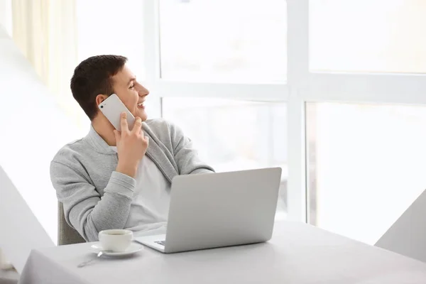 Молодий чоловік розмовляє по телефону під час роботи з ноутбуком в кафе — стокове фото