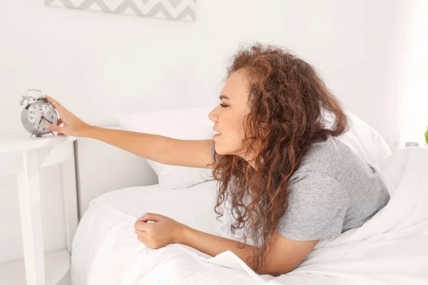 Morning of sleepy young African-American woman turning off alarm clock while lying in bed — Stock Photo, Image