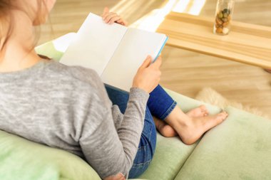 Evdeki kanepede kitap okuyan genç bir kadın.