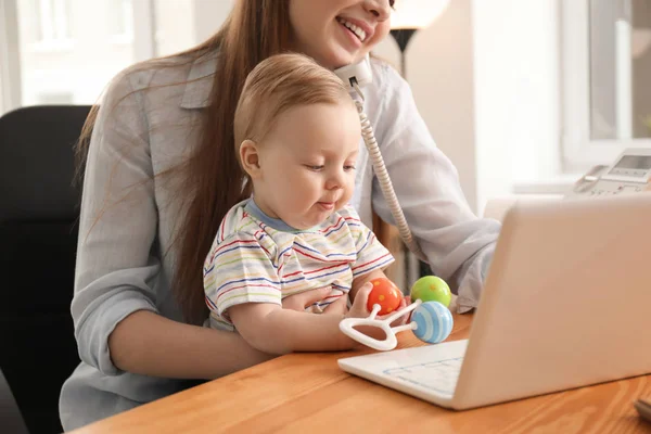 Madre joven con bebé hablando por teléfono mientras trabaja en la oficina — Foto de Stock