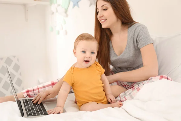 Young mother with baby working on bed at home — Stock Photo, Image