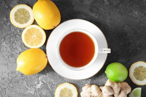 Composition with cup of hot aromatic tea, lemon and ginger on textured table — Stock Photo, Image