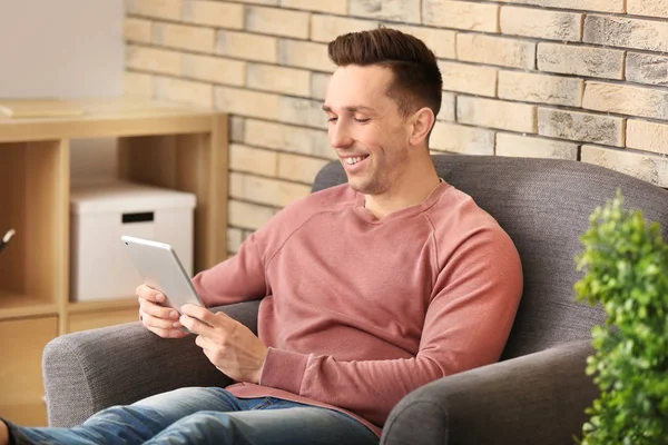 Young man using tablet PC while resting on armchair at home — Stock Photo, Image