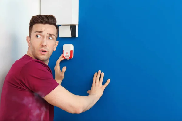 Frightened man using fire alarm system indoors — Stock Photo, Image