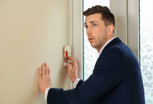 Frightened man using fire alarm system indoors