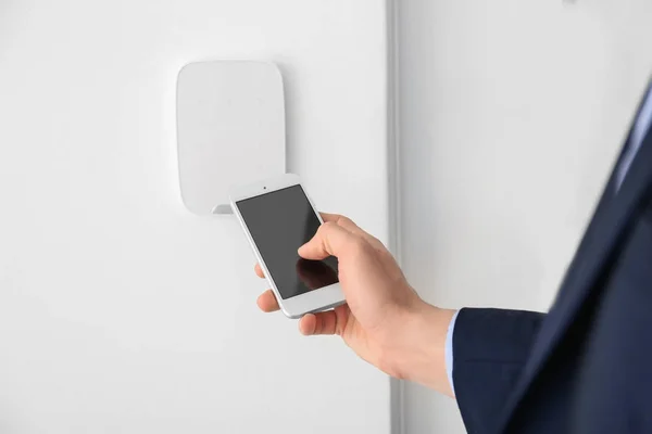 Young man with phone near security system indoors, closeup — Stock Photo, Image