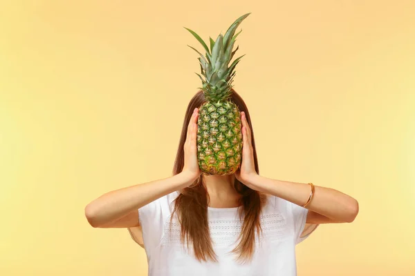 Junge Frau versteckt Gesicht hinter Ananas auf farbigem Hintergrund — Stockfoto