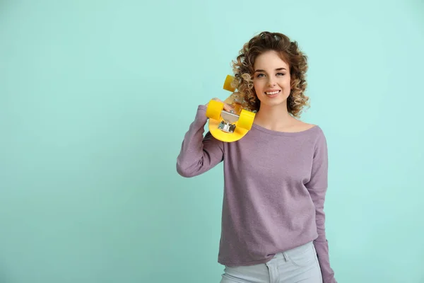 Mooie jonge vrouw met skateboard op kleur achtergrond — Stockfoto