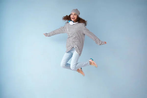 Jumping young woman with headphones on color background — Stock Photo, Image