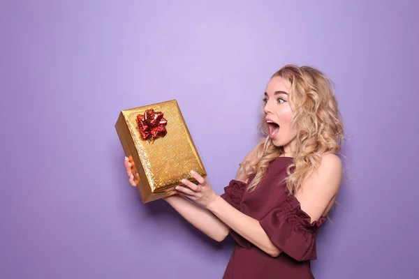 Surprised young woman with gift box on color background — Stock Photo, Image