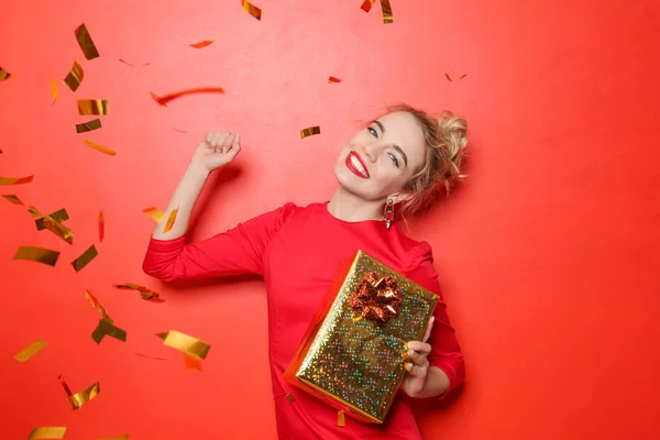 Porträt der schönen jungen Frau mit Geschenkschachtel und fallendem Konfetti auf farbigem Hintergrund — Stockfoto