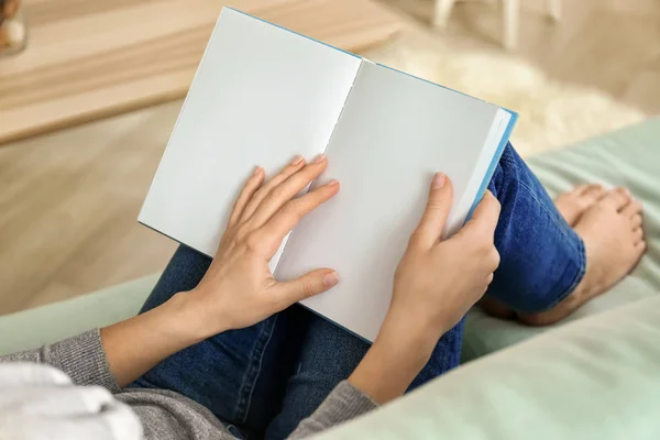 Joven mujer leyendo libro en sofá en casa — Foto de Stock