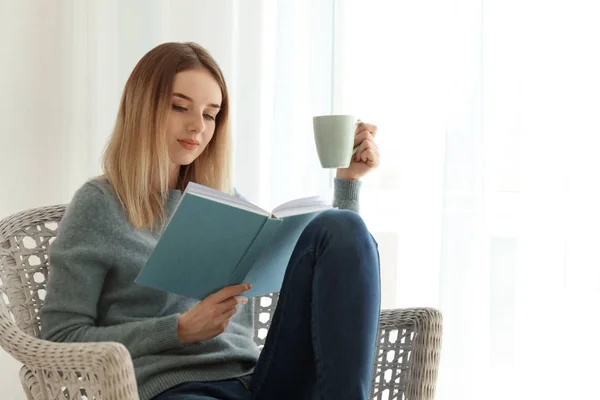 Young woman drinking tea while reading book at home — Stock Photo, Image