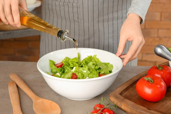 Woman adding olive oil into bowl with fresh vegetable salad on table — Stock Photo, Image