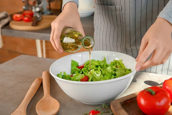 Donna che aggiunge olio d'oliva in ciotola con insalata di verdure fresche sul tavolo — Foto Stock