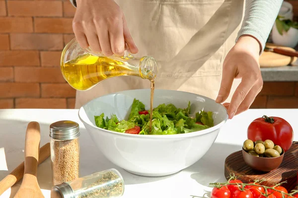 Vrouw toevoegen van olijfolie in de kom met verse fruit salade op tafel — Stockfoto