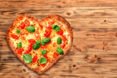 Ahşap arka planda kalp şeklinde lezzetli bir pizza.