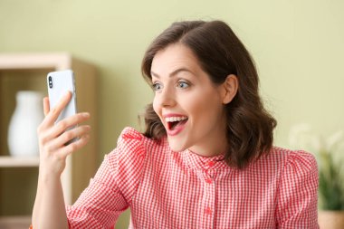 Evde cep telefonu olan şaşırmış genç bir kadın.