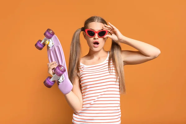 Surprised young woman with skateboard on color background — Stock Photo, Image