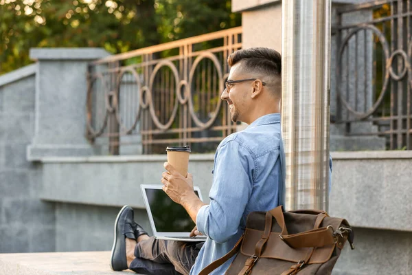 Портрет красивого бизнесмена с ноутбуком и чашкой кофе на открытом воздухе — стоковое фото