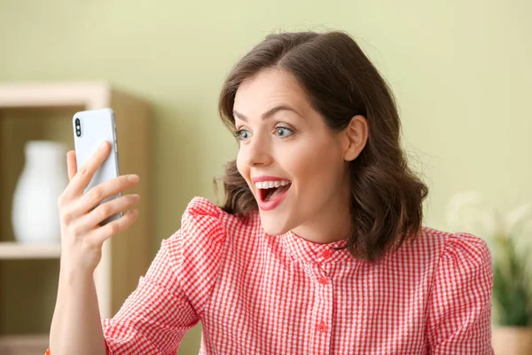 Surprised young woman with mobile phone at home — Stock Photo, Image