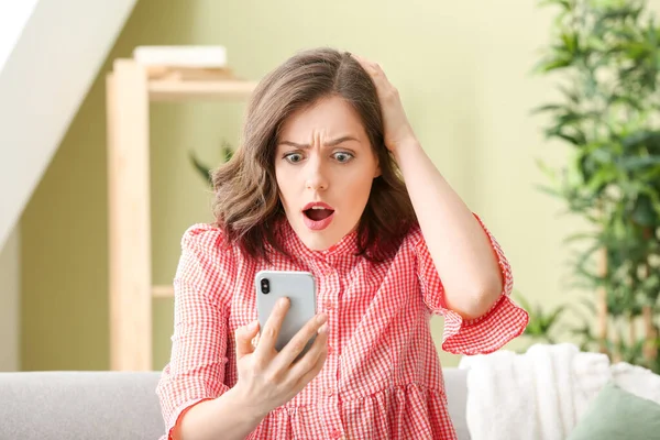 Mujer joven sorprendida con teléfono móvil en casa —  Fotos de Stock