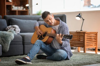 Yakışıklı adam evde gitar çalıyor.