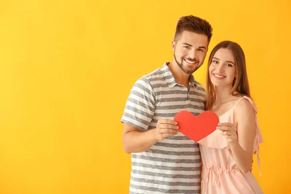 Porträt eines glücklichen jungen Paares mit Papierherz auf farbigem Hintergrund — Stockfoto