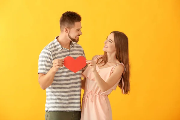 Portrait of happy young couple with paper heart on color background — ストック写真