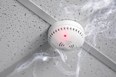 Modern smoke detector in action on ceiling indoors