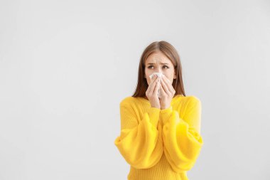 Young woman suffering from allergy on light background