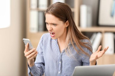 Stressed young woman with mobile phone in office