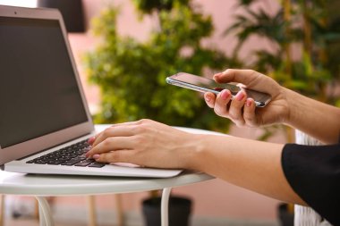 Bilgisayarlı bir kadın masada cep telefonu kullanıyor, yakın plan.