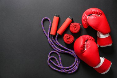 Boxing gloves, wrist bands and jumping rope on dark background clipart