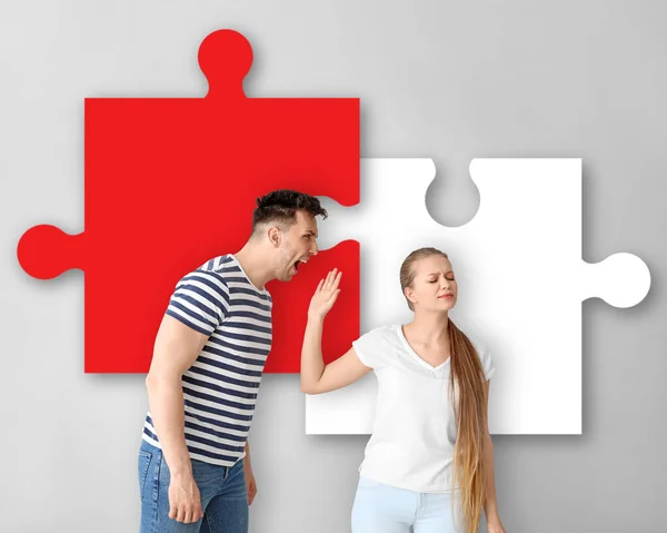 Young quarrelling couple and pieces of puzzle on light background — Stock Photo, Image