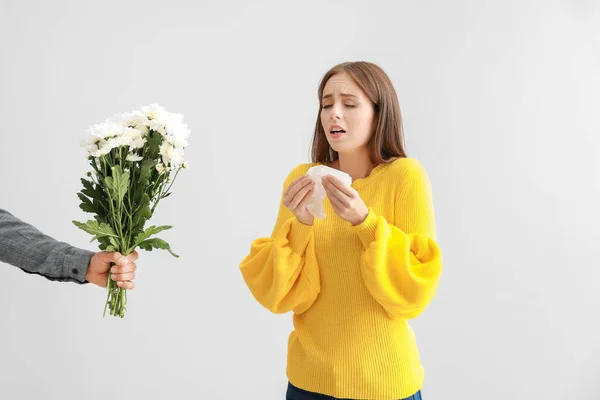 Man giving flowers to young woman suffering from allergy on light background — Stock Photo, Image