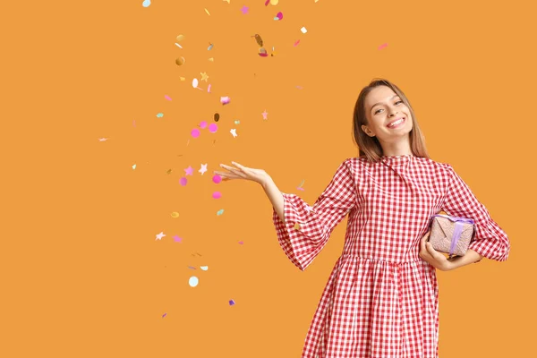Gyönyörű nő ajándék doboz és konfetti a színes háttér — Stock Fotó